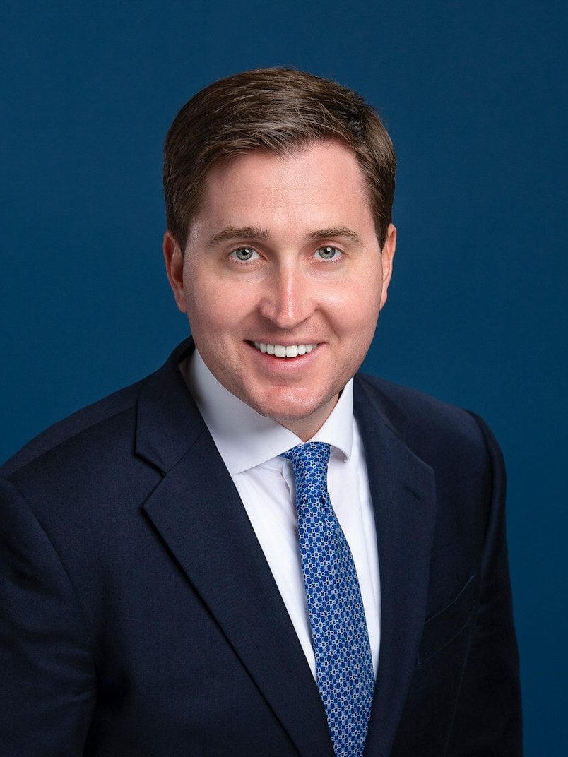 smiling professional headshot in a navy suit with blue tie