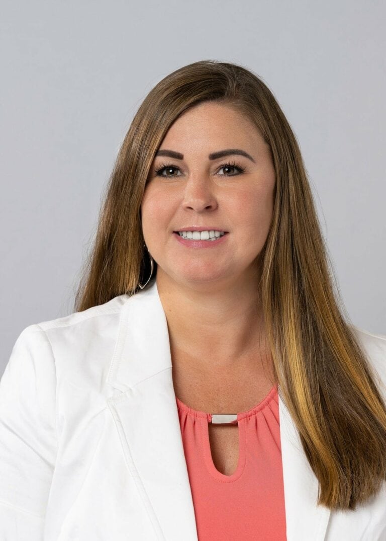 female with long brown hair in a white blazer and pink shell