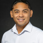 Professional headshot of Hispanic man in white dress shirt with friendly smile on black background